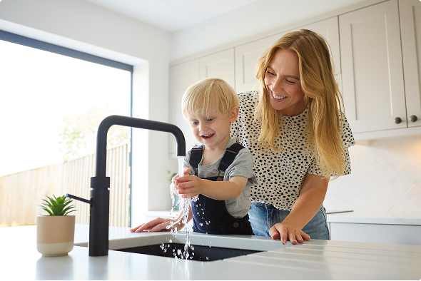 Kind wast zijn handen in de keuken terwijl moeder toekijkt